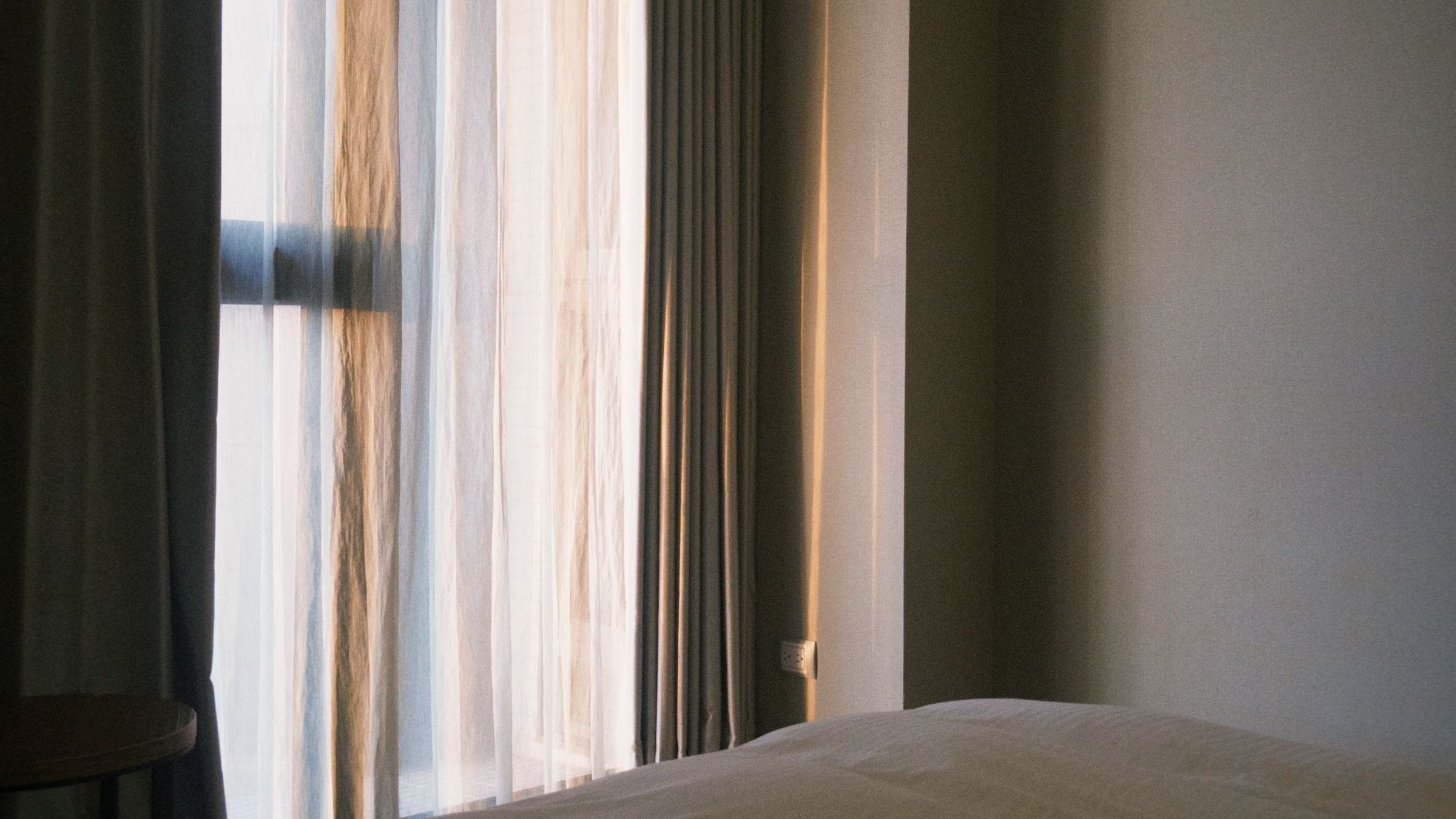 Warm evening light falling across a bed through a curtained window