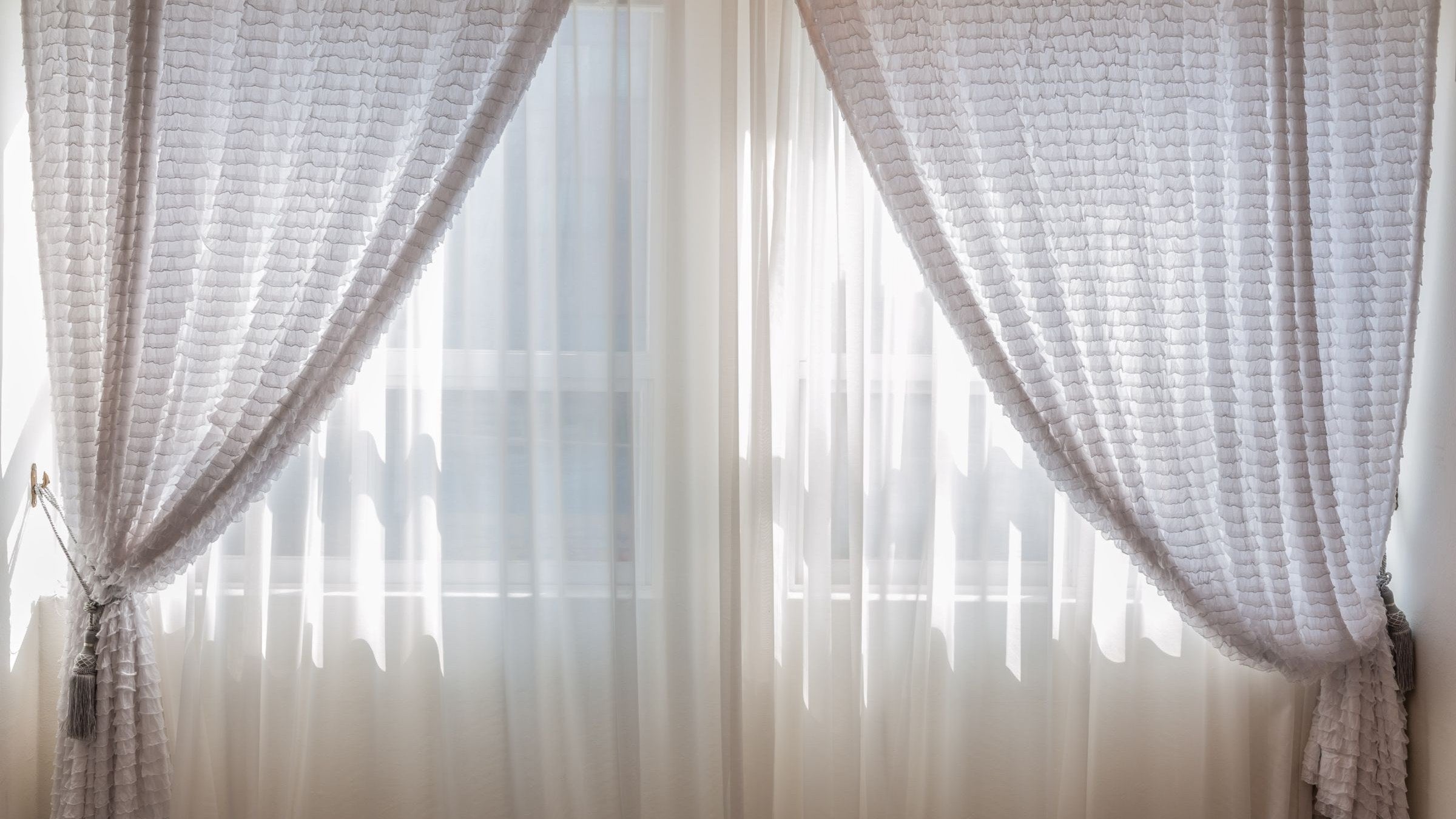 Pale curtains drawn across a bright window to keep the sun out of a bedroom