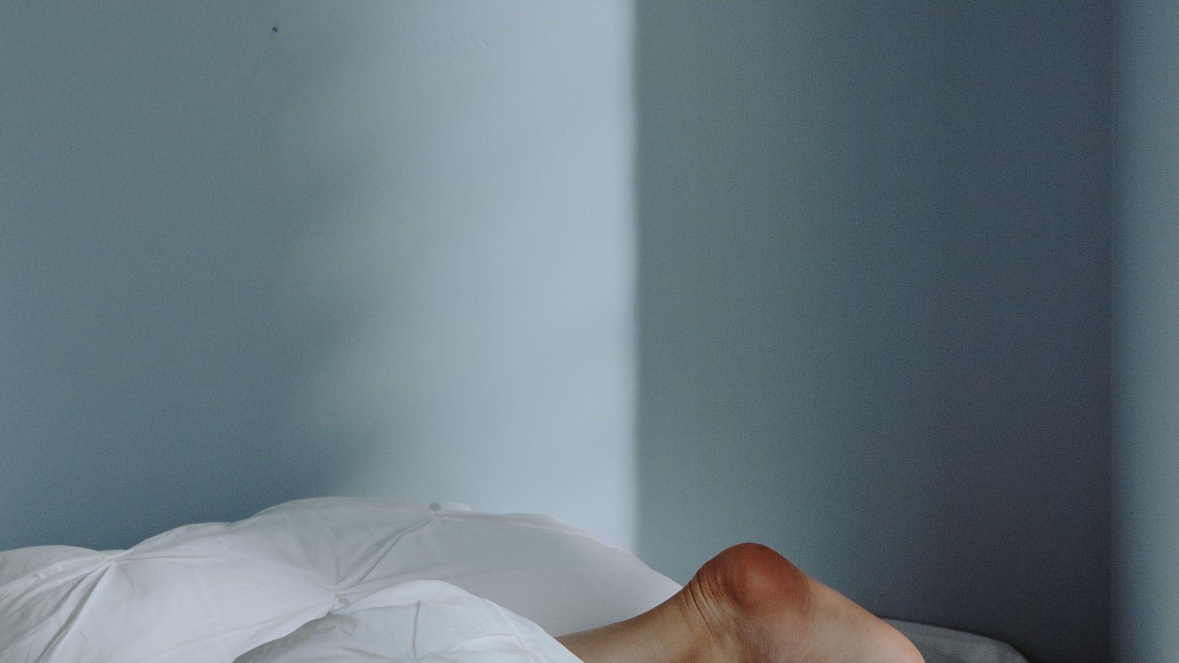 Bare feet pushed out from under a white duvet to shed heat