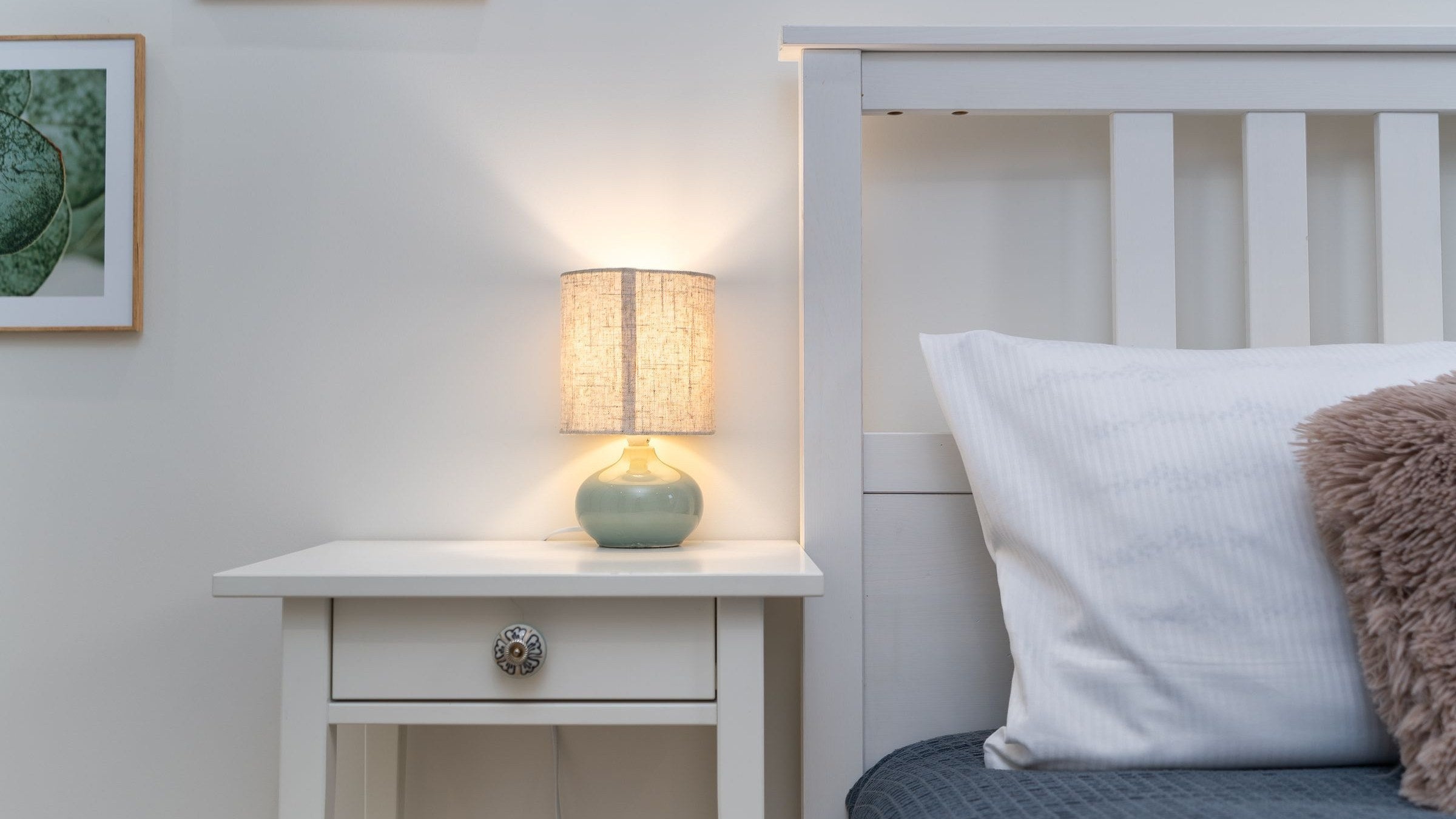 A bedside lamp switched on beside a made bed in the middle of the night