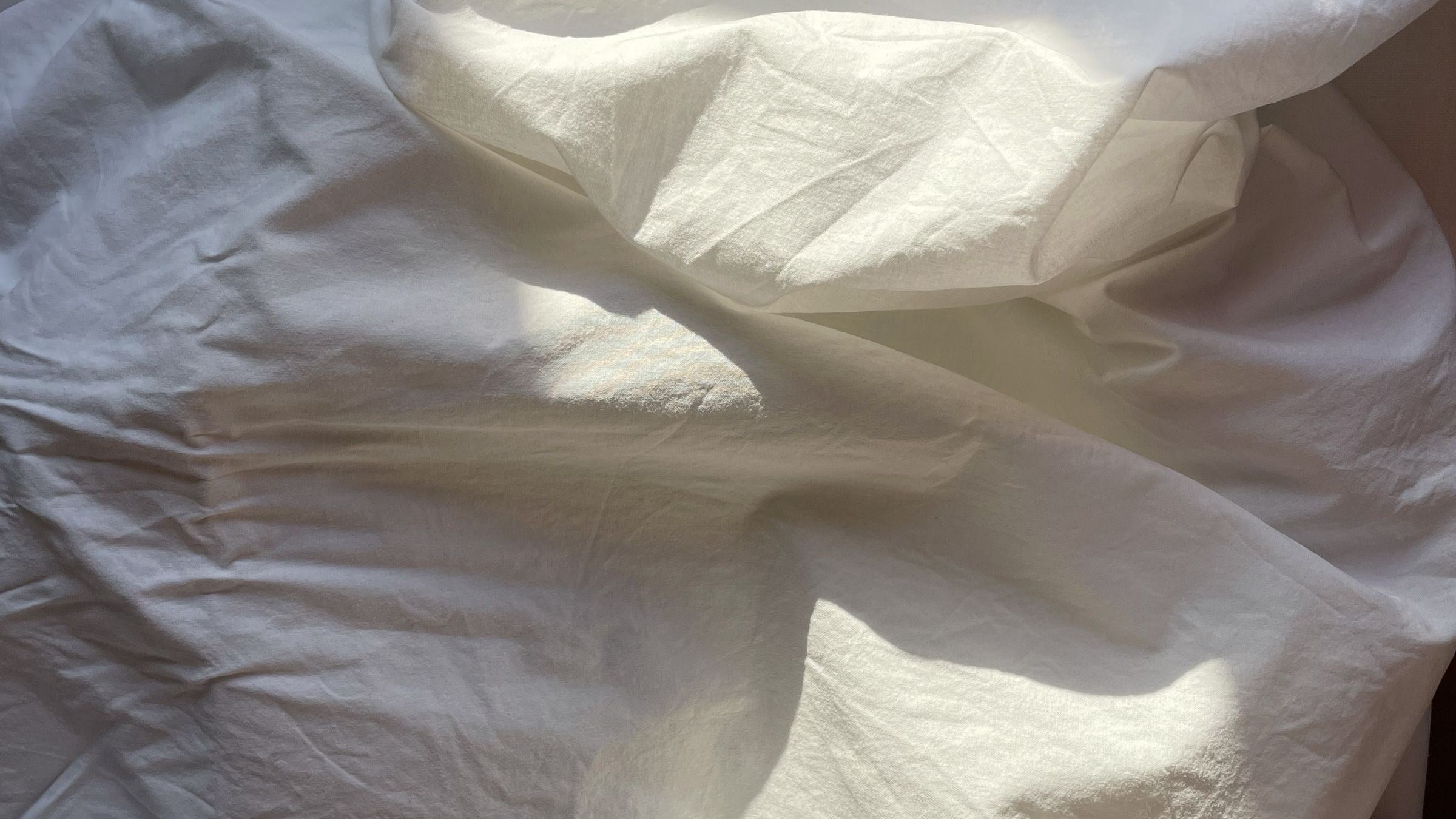 Morning sunlight falling across crumpled white bed sheets