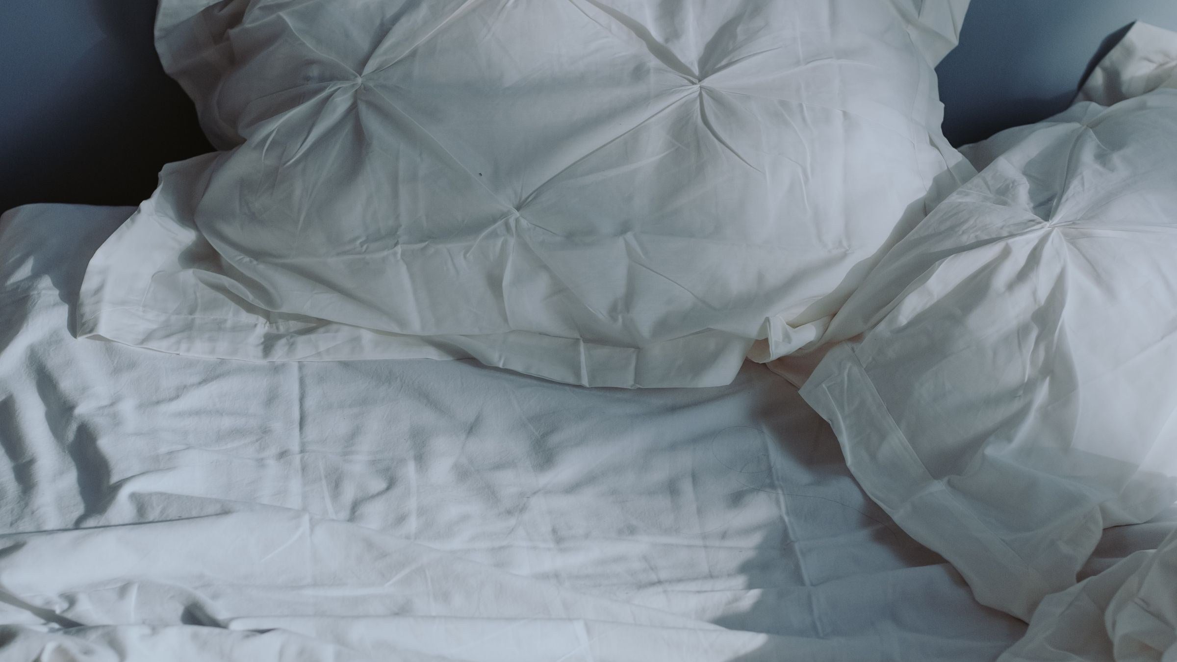 Soft white pillows on an unmade bed in morning light